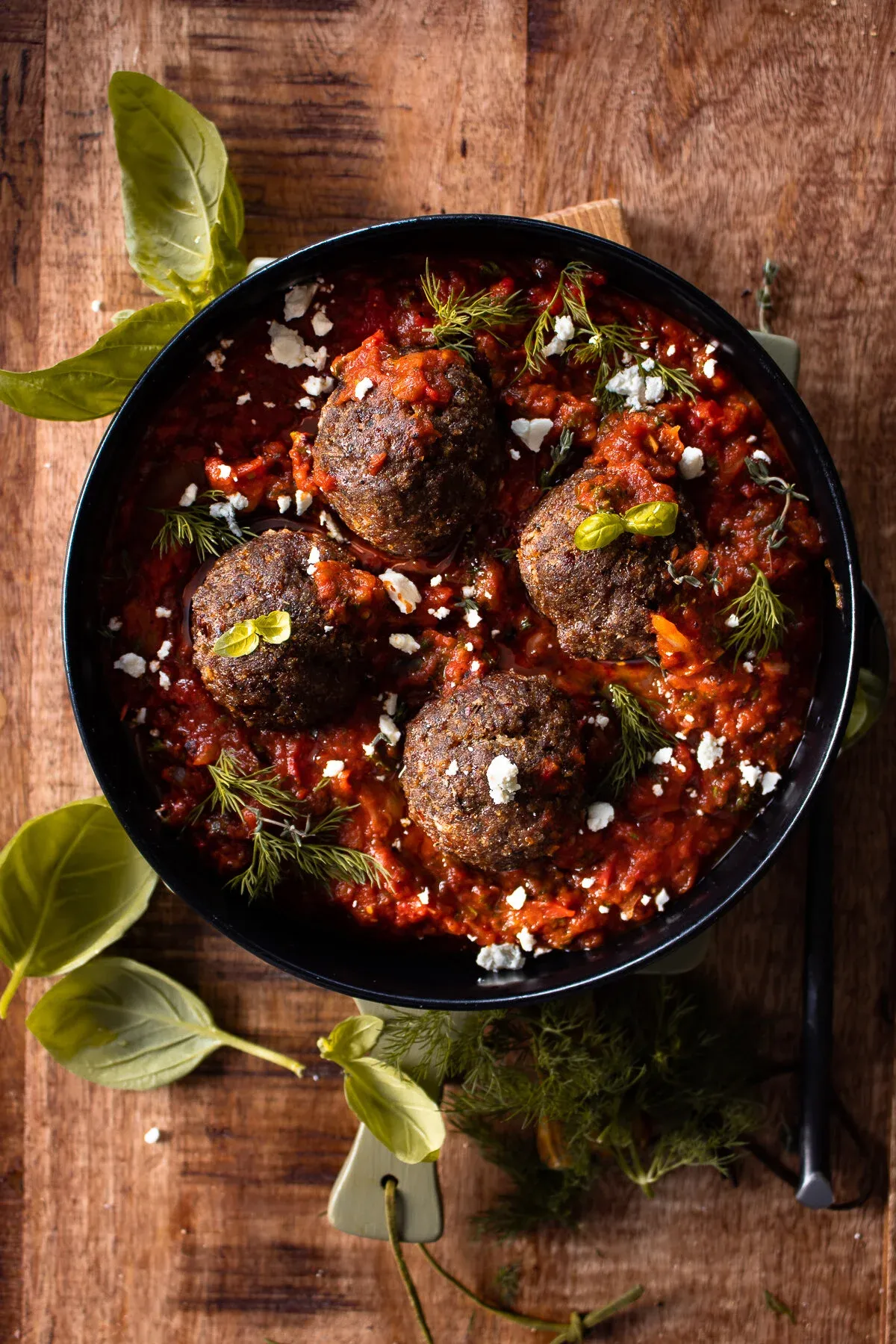 Four large herb-seasoned beef meatballs nestled in a deep, chunky spicy tomato sauce inside a black skillet