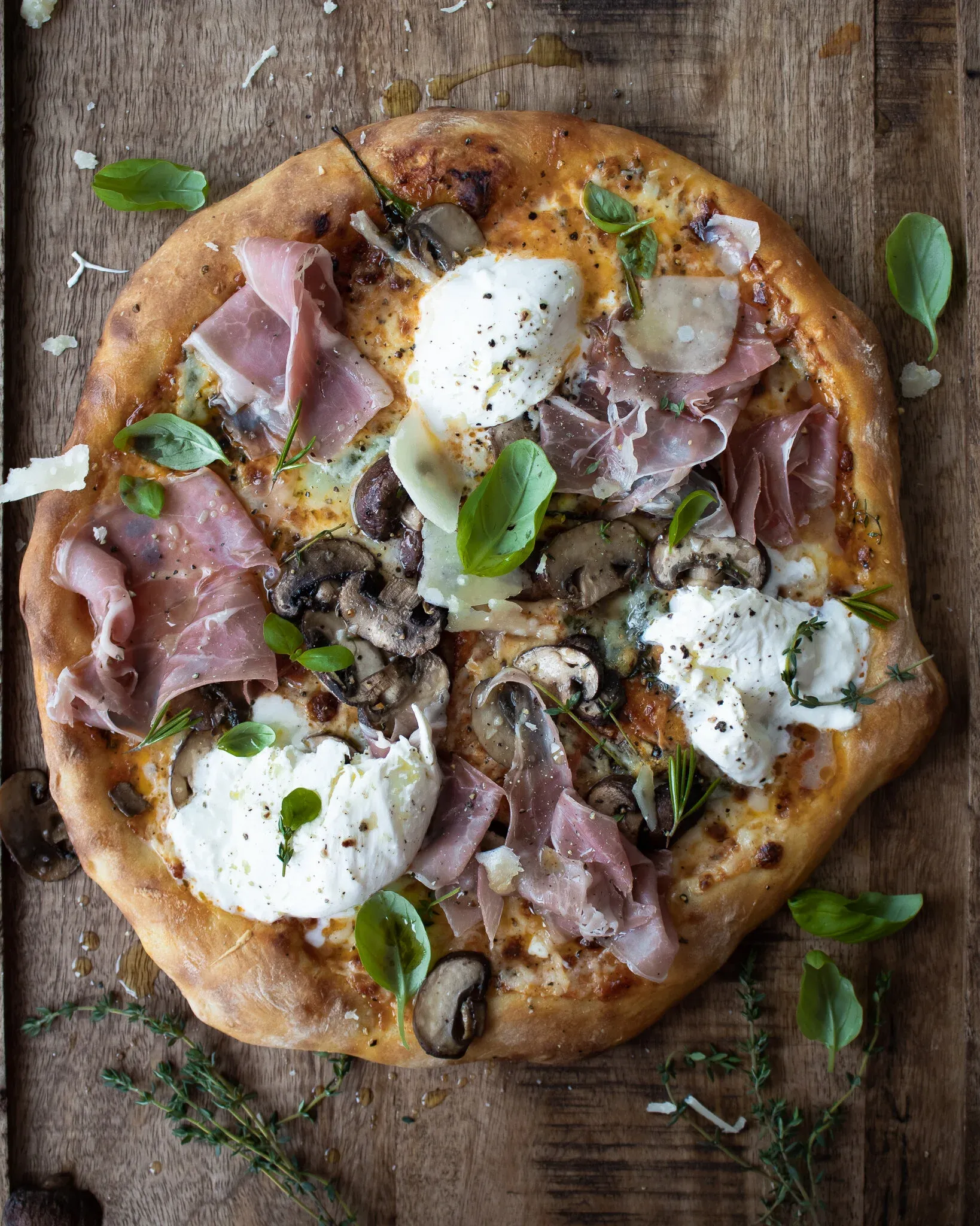 Overhead view of a whole Roasted Mushroom and Prosciutto Pizza on a rustic wooden board