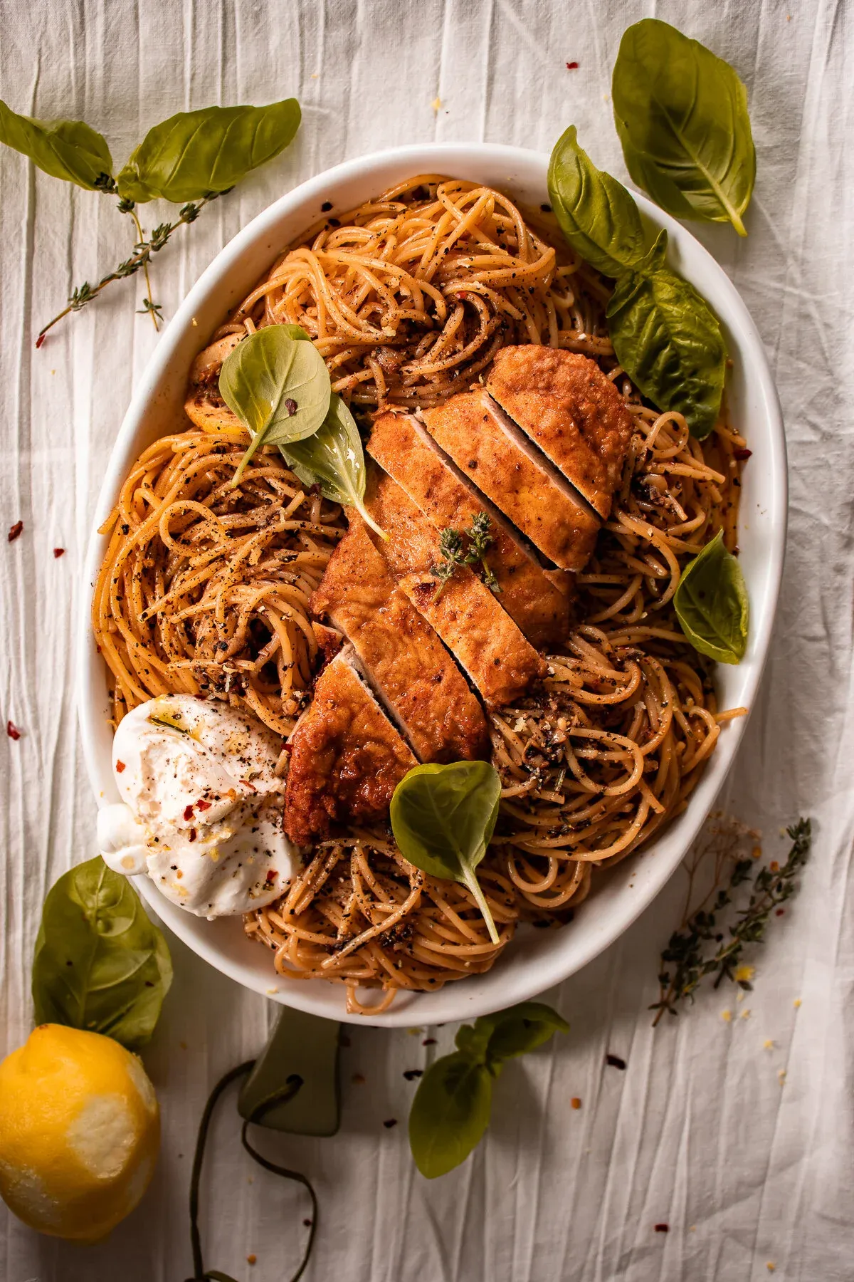 White oval serving dish of lemon pepper chicken pasta with burrata