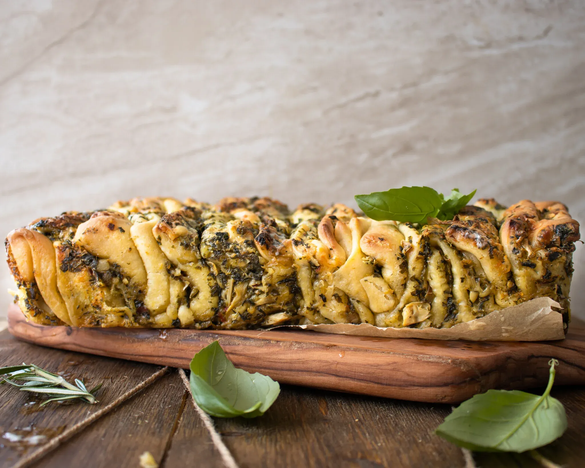 Pesto spinach and artichoke pull-apart bread served whole on a rectangular wooden board lined with parchment paper