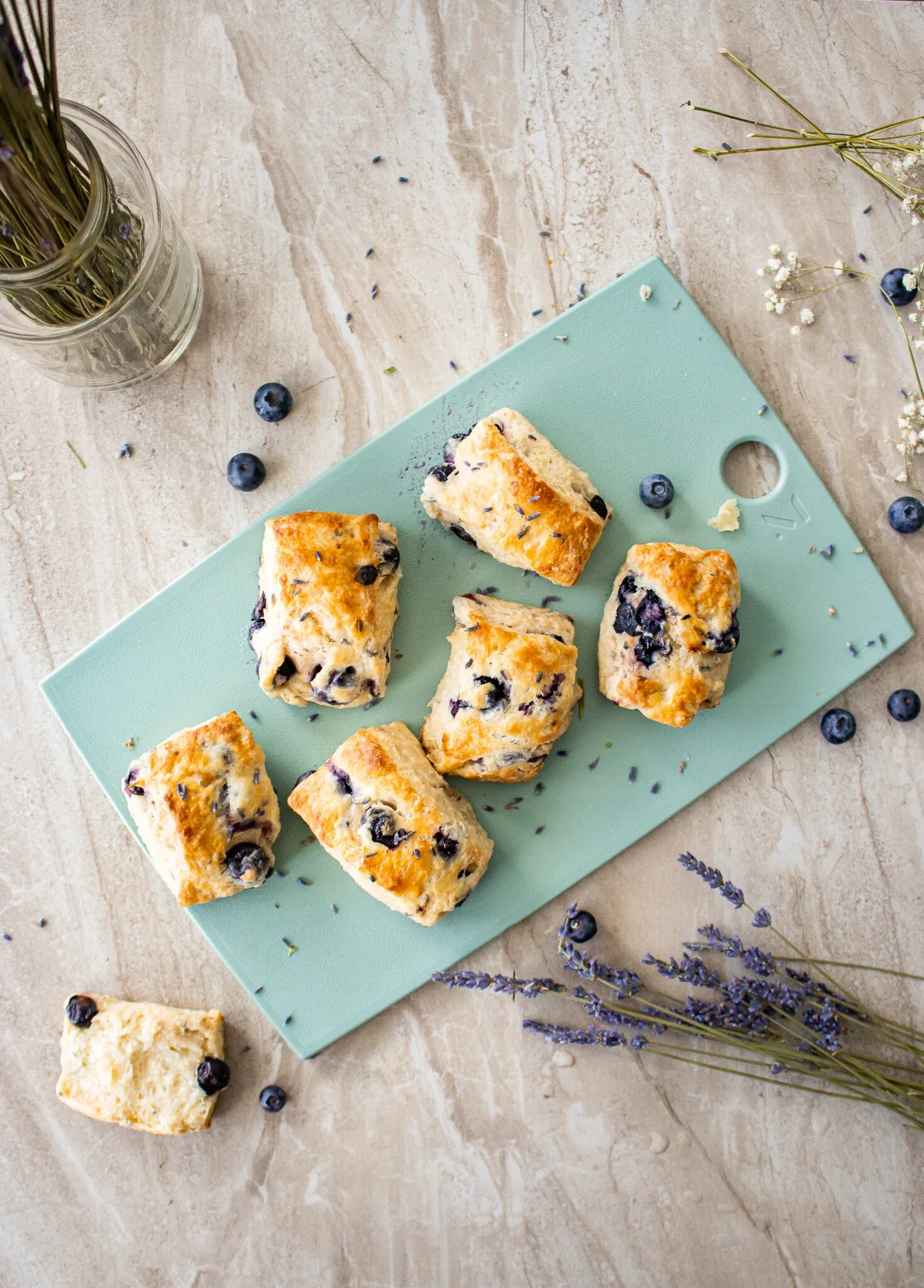 Overhead flat-lay of six golden-baked Blueberry Lavender Buttermilk Biscuits arranged on a mint-green cutting board