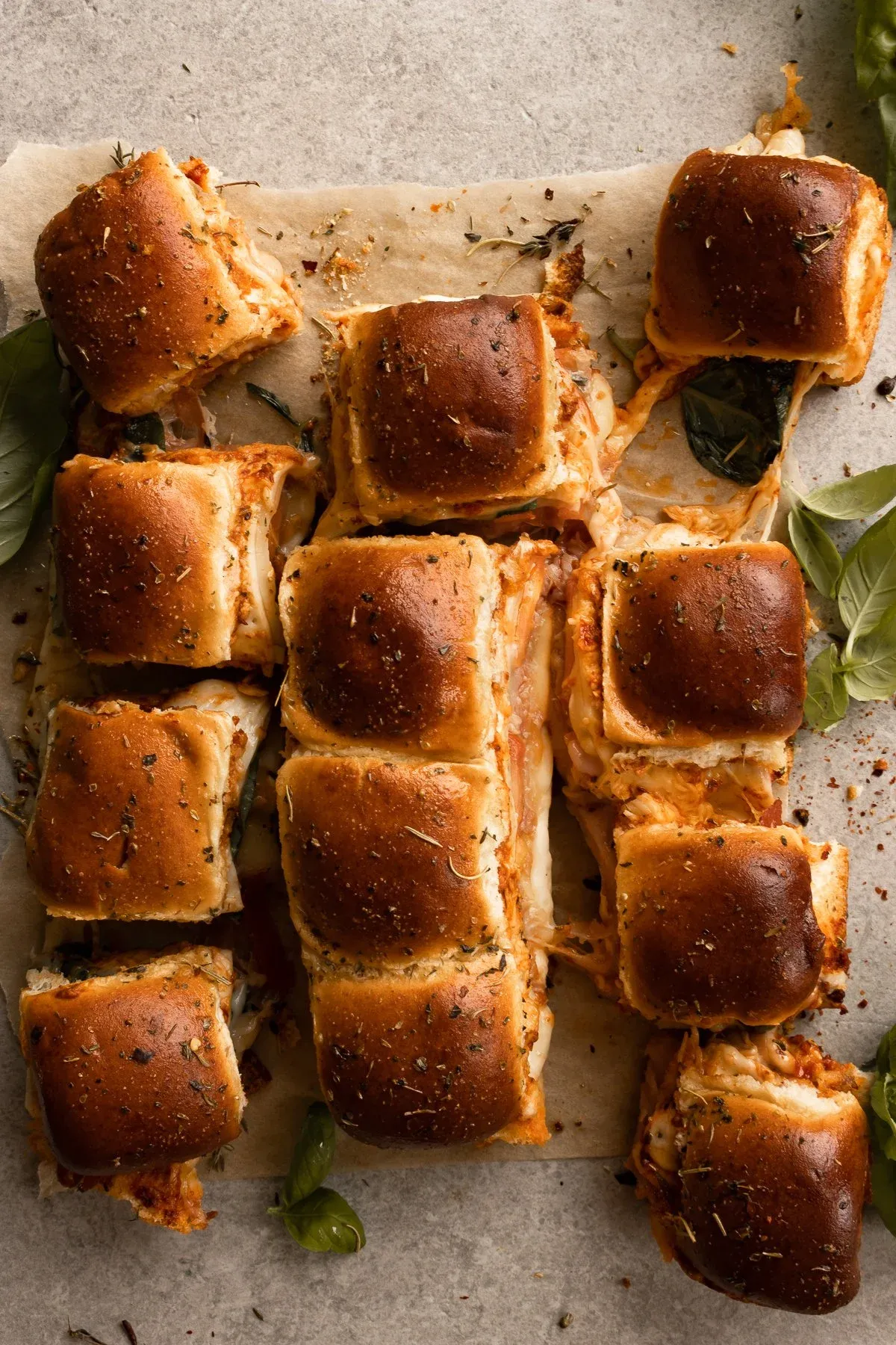 Overhead flat-lay of prosciutto and cheese pull-apart sliders on parchment paper on a light gray surface