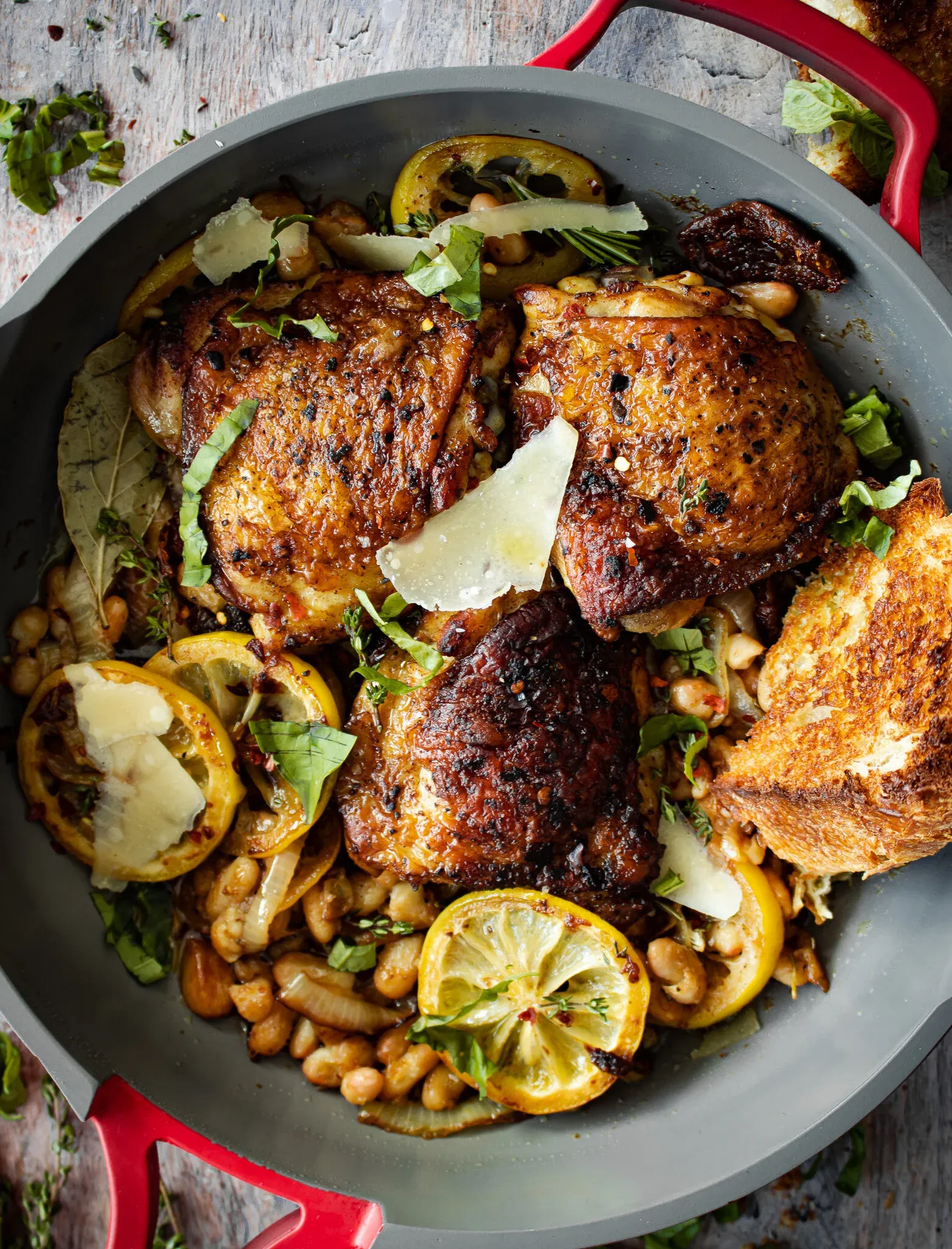 Oven Roasted Chicken with White Beans and Sundried Tomatoes in a gray Staub-style braiser with bright red handles