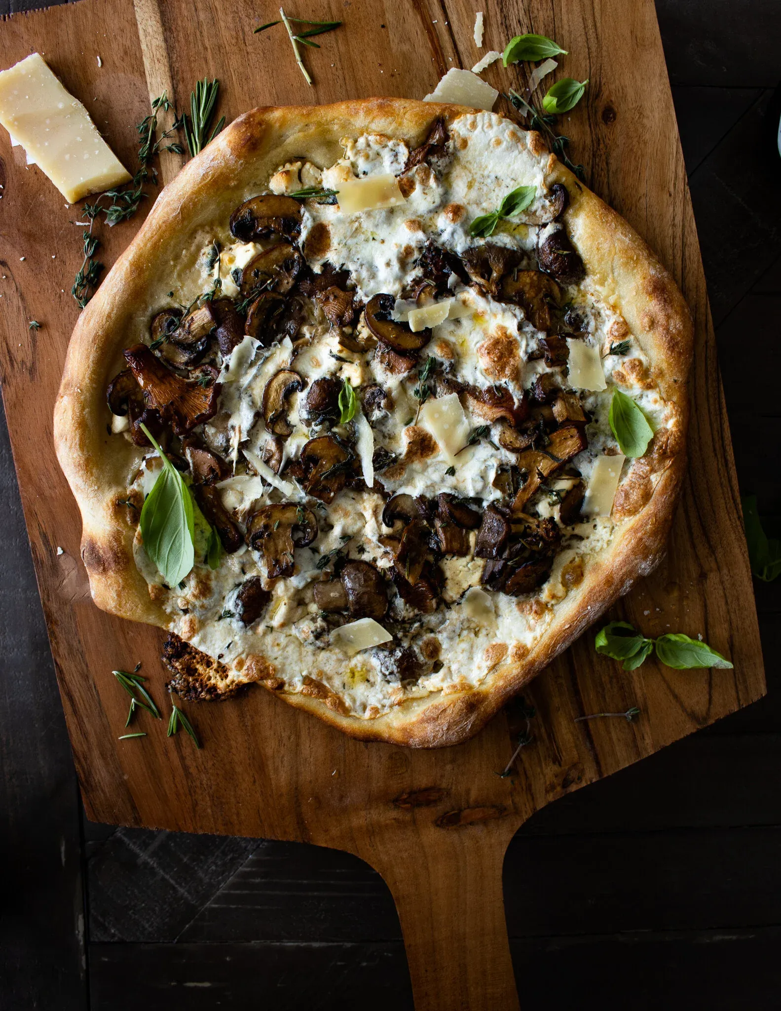 Mushroom and Goat Cheese Pizza on a wooden pizza peel, the puffy charred artisan crust topped with creamy goat cheese