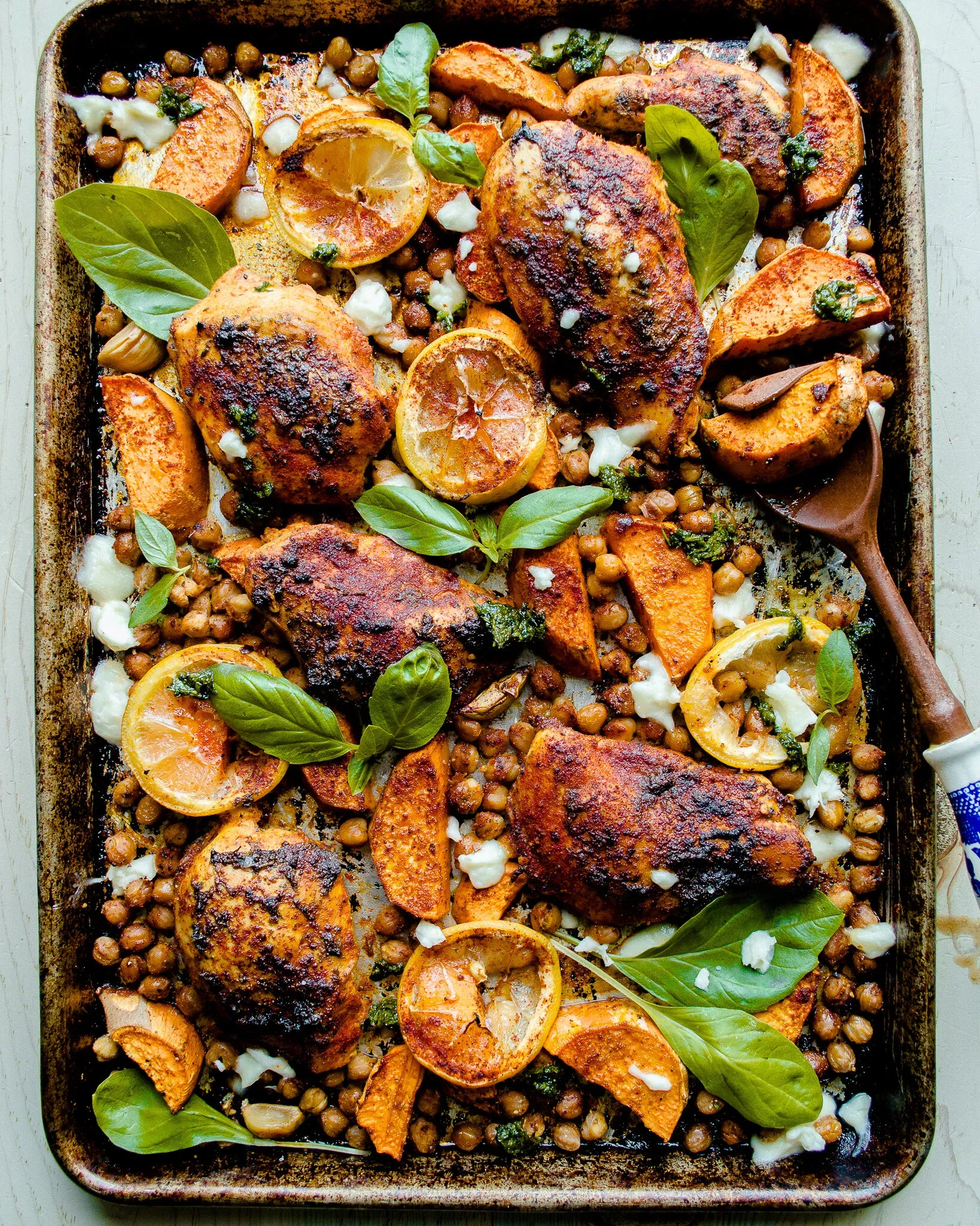 Overhead view of a dark sheet pan of Sheet Pan Harissa Chicken with Sweet Potatoes and Chickpeas