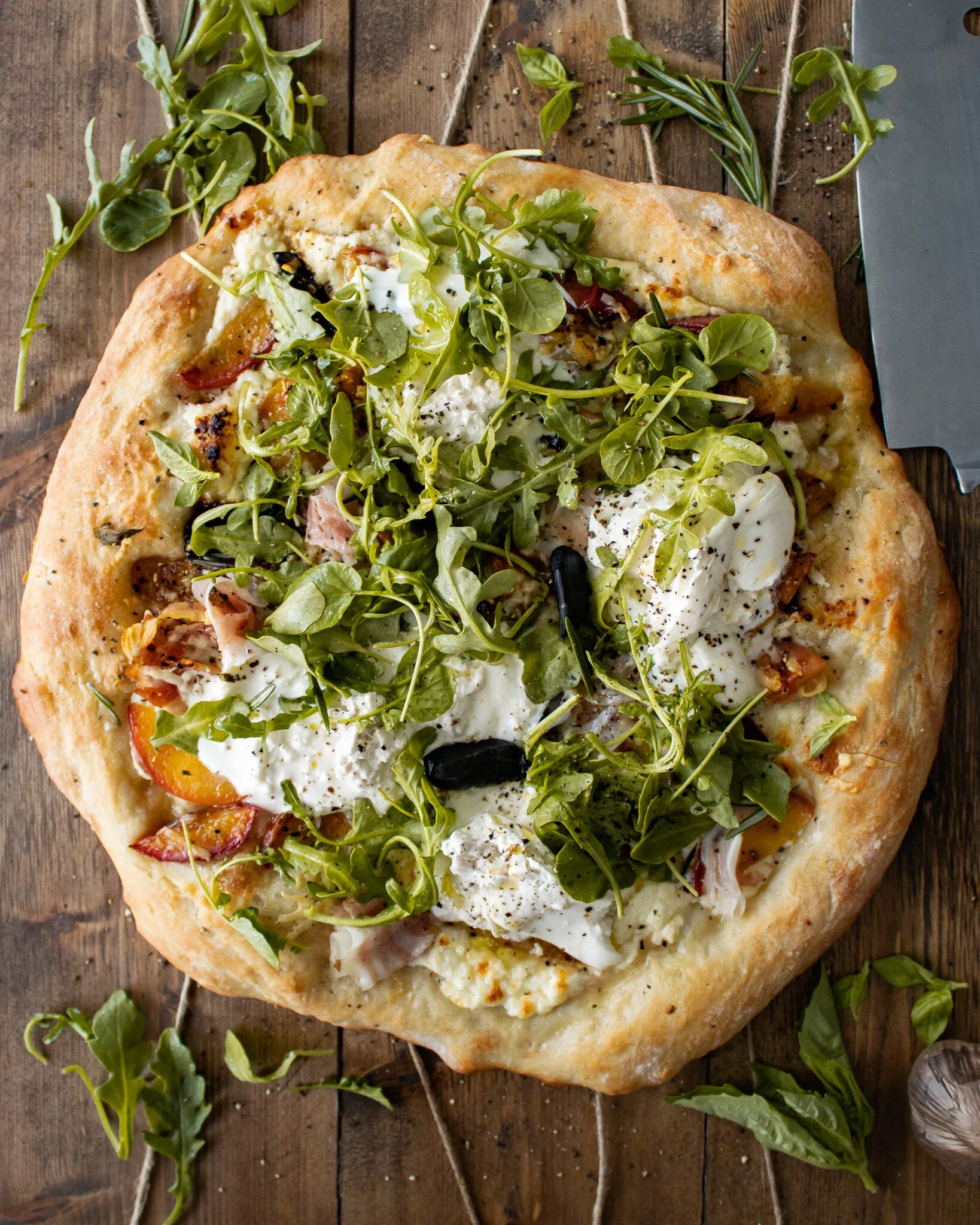 Overhead close-up of a whole Burrata and Rosemary Peach Pizza on a dark wood board