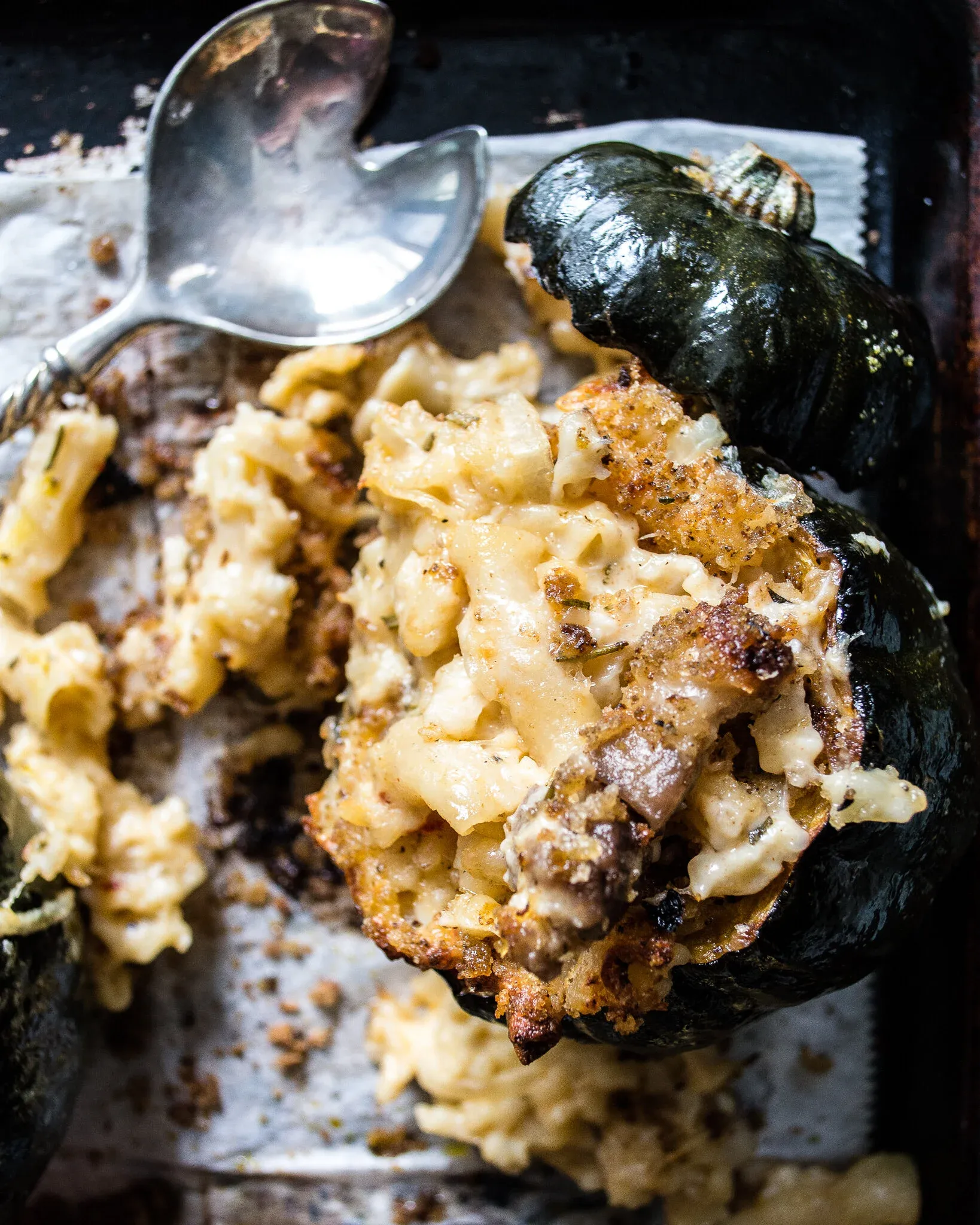 Close angled overhead shot of a dark baking sheet with a deeply roasted dark green acorn squash half overflowing with Crab Mac and Cheese