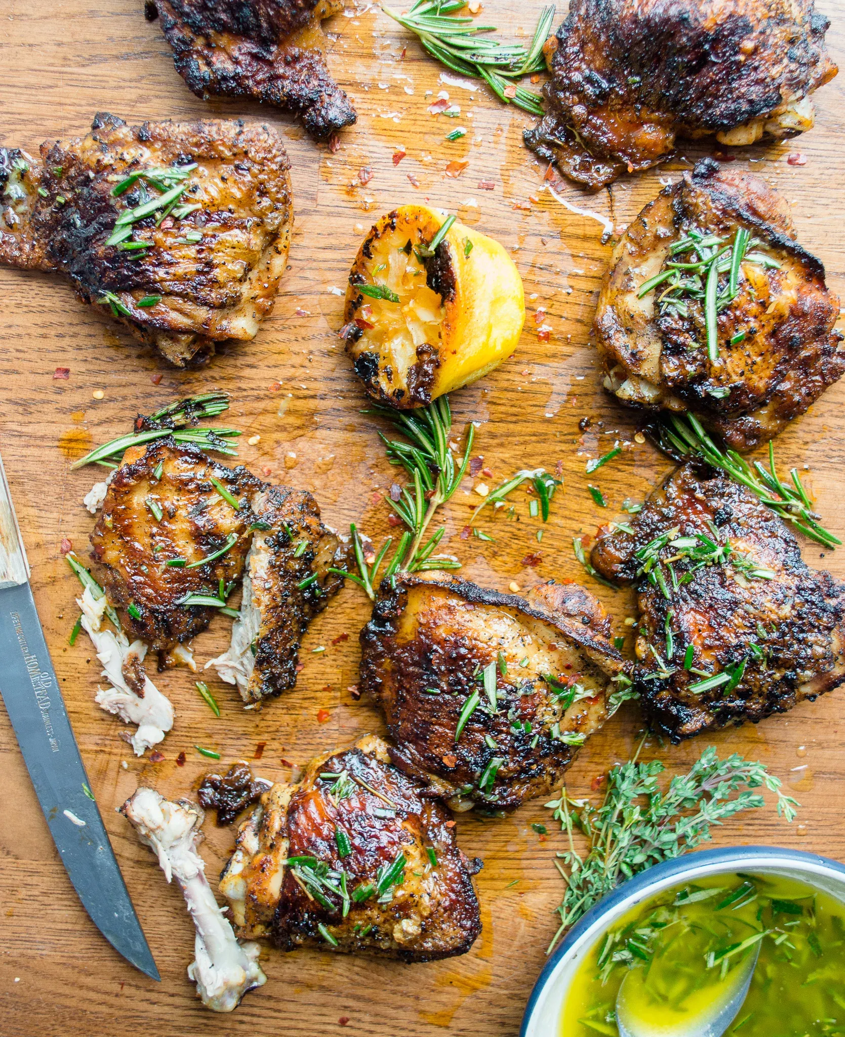 Overhead flat-lay of eight cast iron grilled chicken thighs on a large wooden cutting board