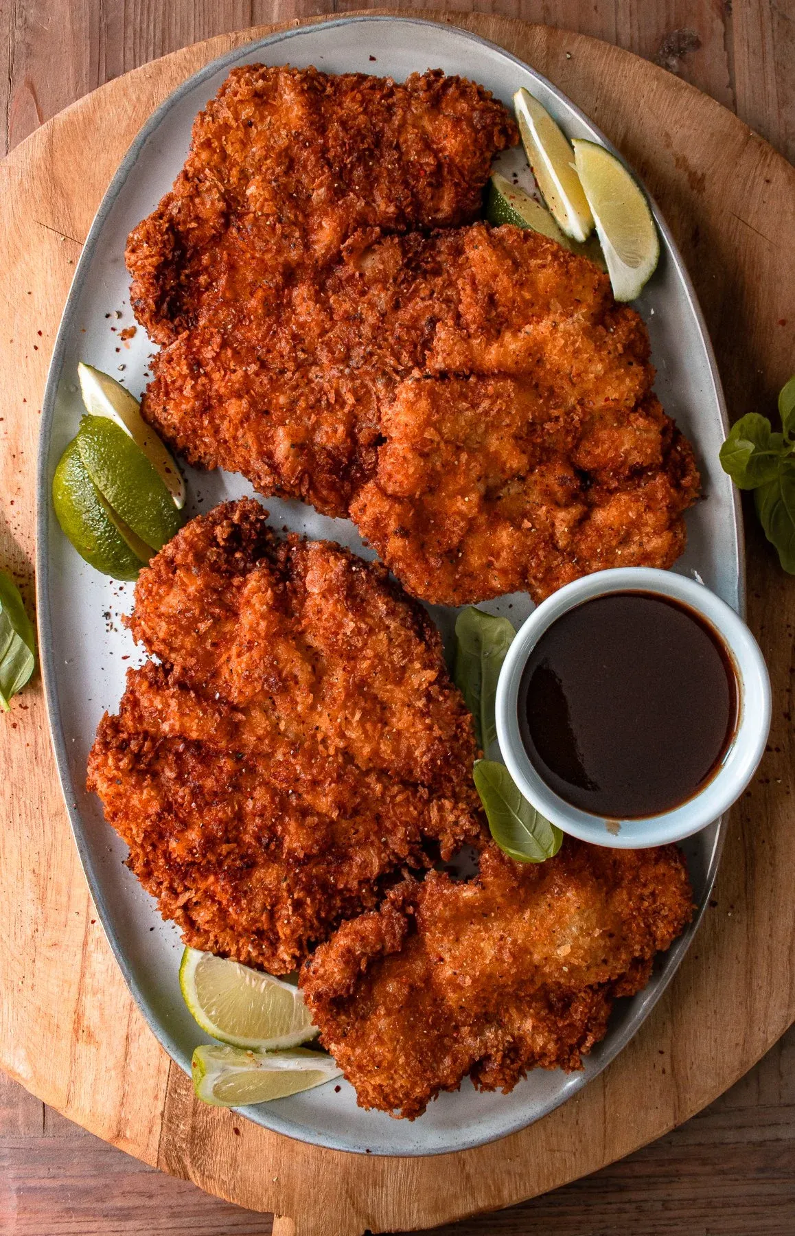 Overhead view of two large mojo chicken katsu cutlets on a grey oval ceramic platter on a round wooden cutting board