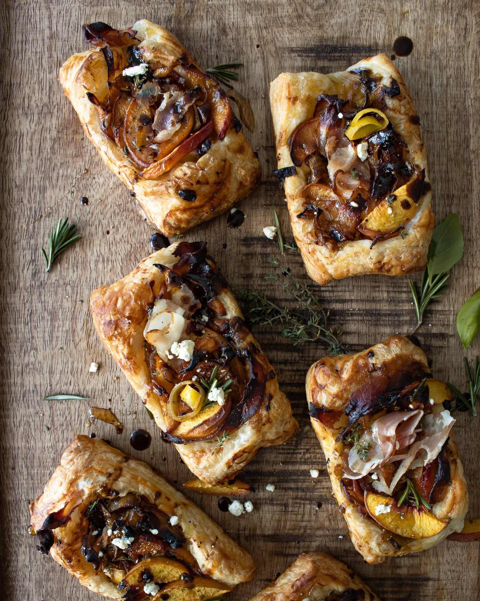 Five caramelized leek and peach puff pastry tarts scattered casually on a rustic wooden cutting board