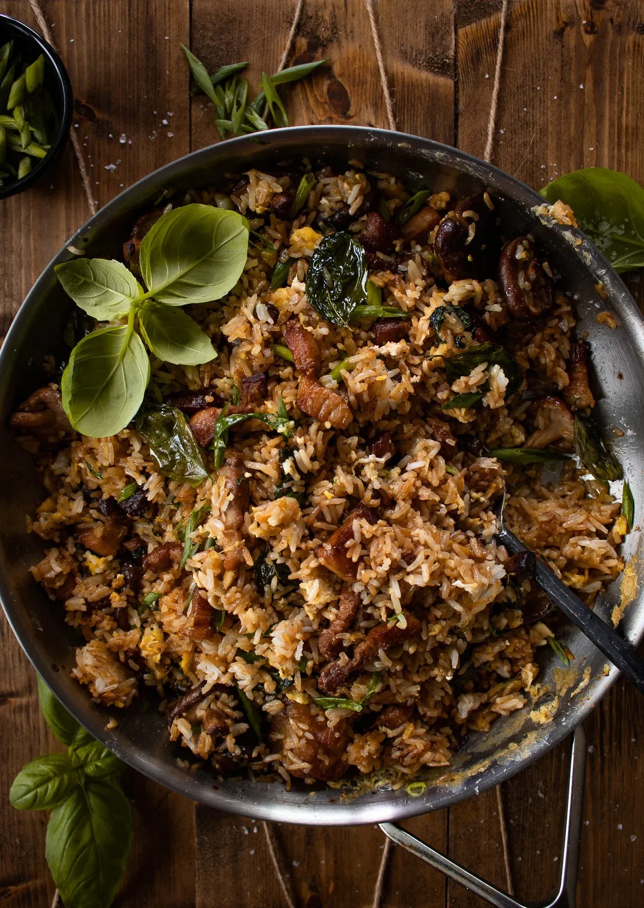 Overhead close-up of pork belly, mushroom and crispy basil fried rice filling a large stainless steel sauté pan