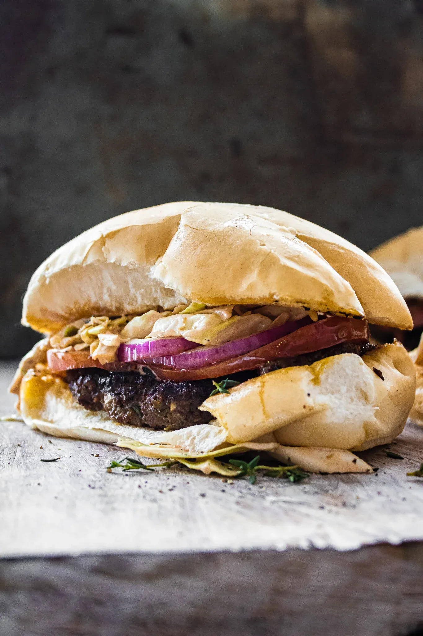 Dominican Chimi Burger served on a soft white pan de agua roll stuffed with a thick charred beef patty, sliced ripe tomato