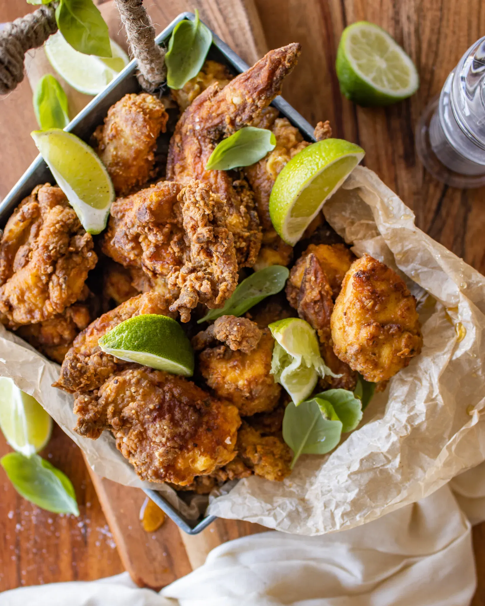 Angled overhead view of pica pollo Dominican fried chicken piled in a square metal tray lined with crumpled parchment paper